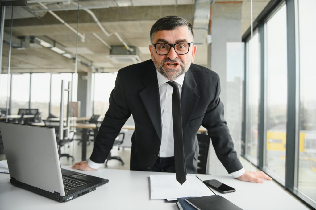 Angry businessman sitting at the table and screaming over.