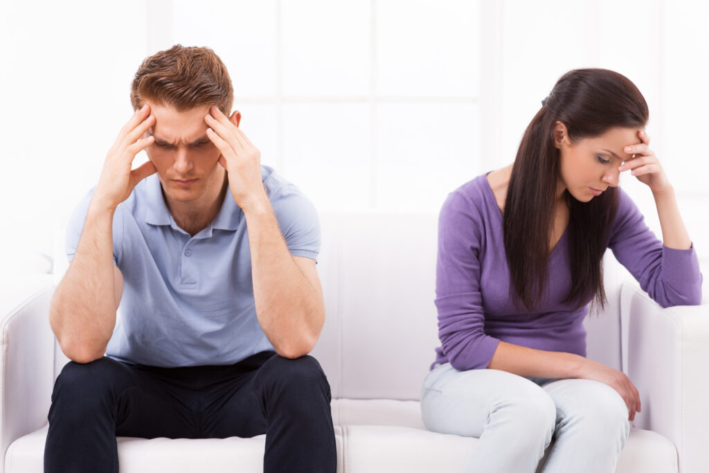 Relationship difficulties. Depressed young man and woman sitting close to each other on the couch and holding head in hands